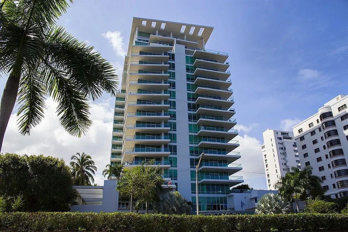 Modern high-rise apartment building with blue balconies and palm trees in front