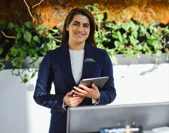 Smiling professional holding a tablet at a reception desk with green plants in the background