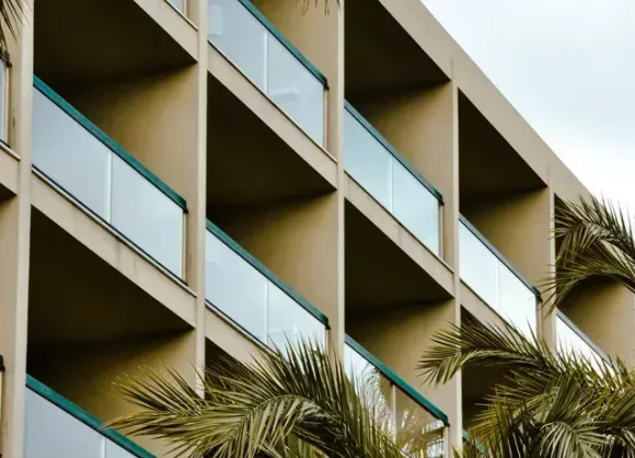 Modern apartment building with balconies and palm trees against a pale sky