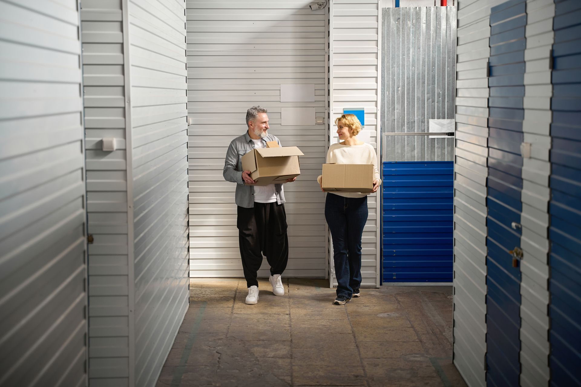 A man and a woman are carrying boxes in a hallway.