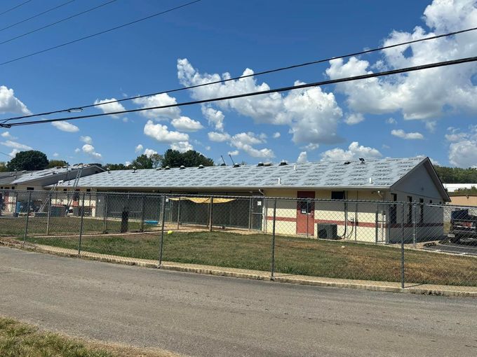 Single-story building with a fenced yard under a blue, cloudy sky beside a road