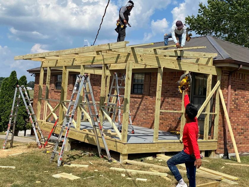 Workers installing a roof on a house under construction, with ladders and scaffolding on the sides.