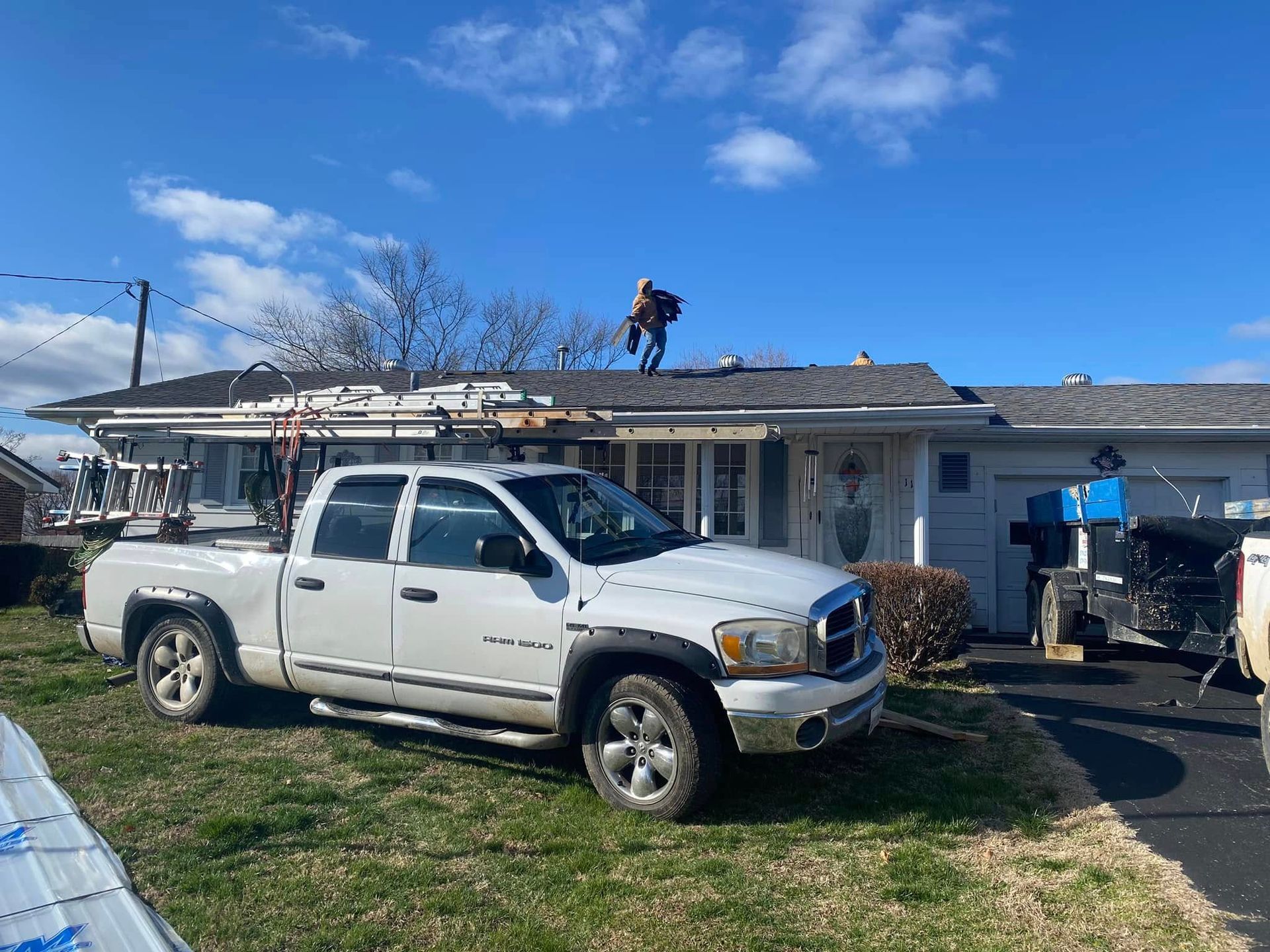 Workers on a roof above a white pickup truck at a house under repair on a sunny day