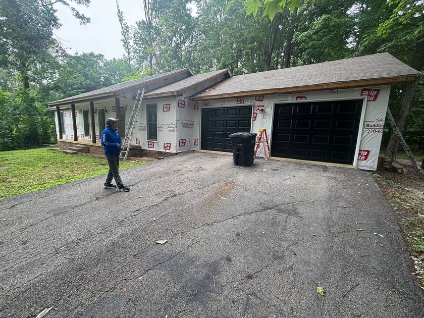 Person walking on a gravel driveway in front of a house under construction, with two garage doors visible.