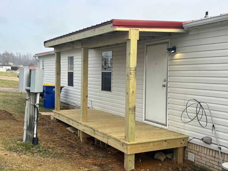 Small raised porch with a red roof and beige siding beside a white house.