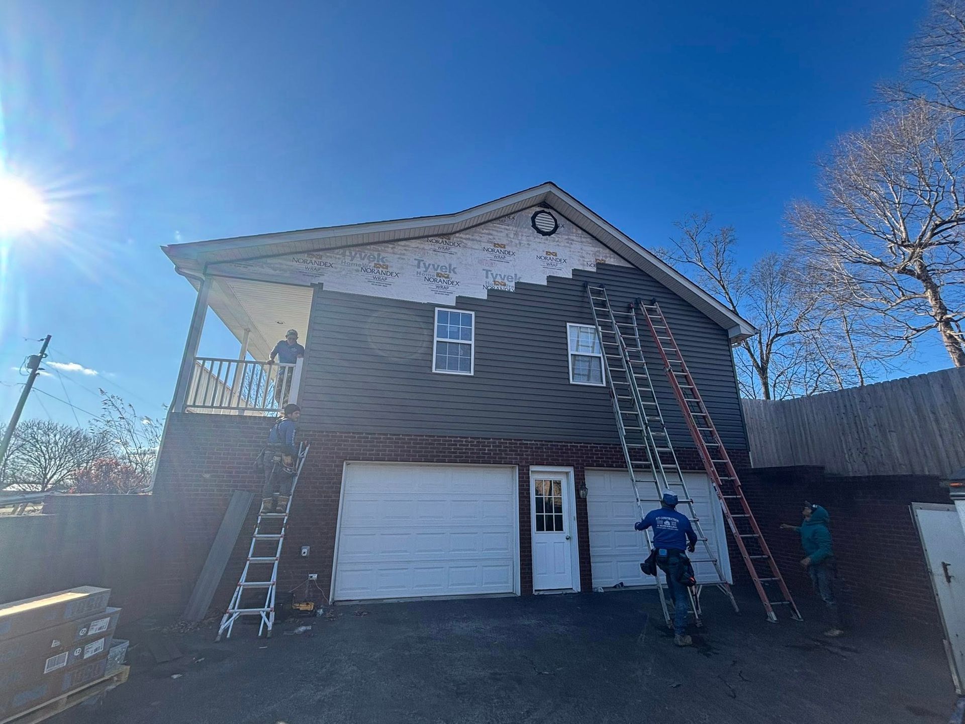 Two-story house with ladders on both sides and a worker at the right side of the driveway.