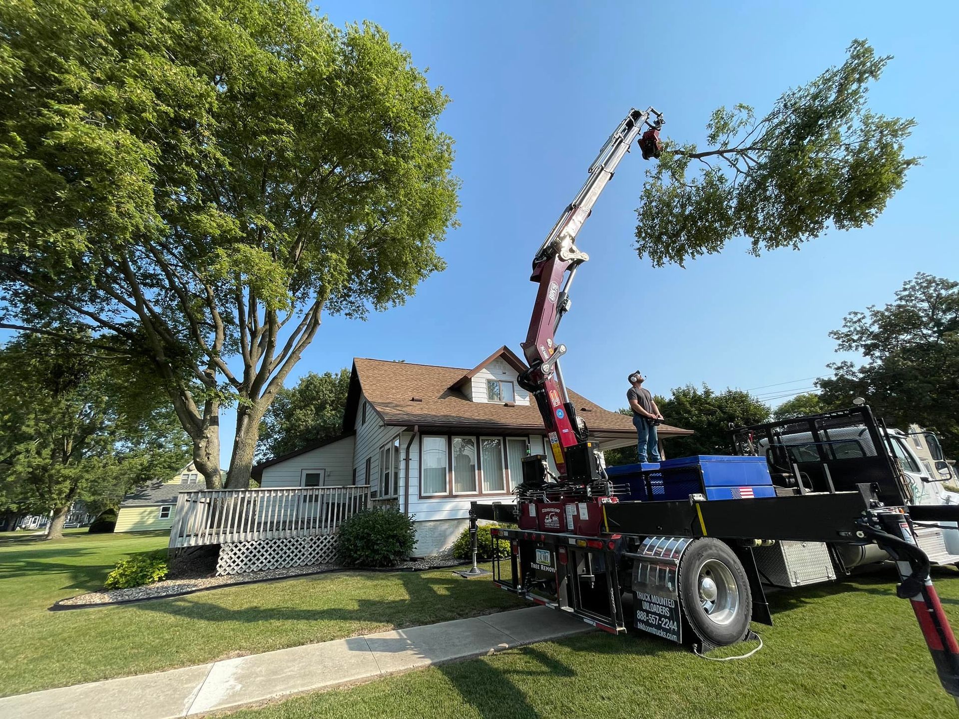 Tree removal crew using a crane truck beside a house on a sunny residential street
