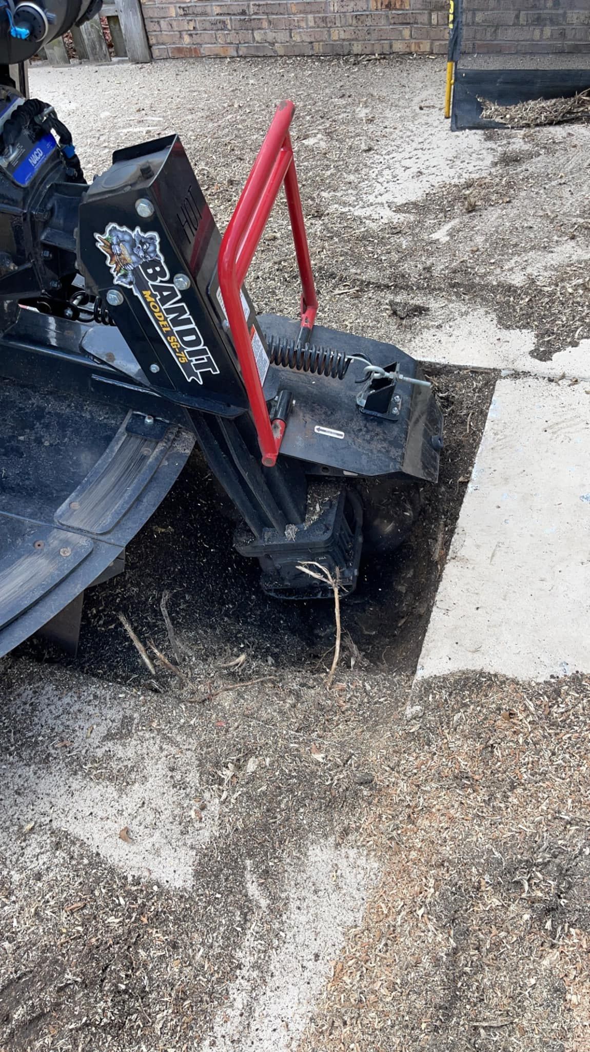 A stump grinder removing a tree stump from gravel next to a building.