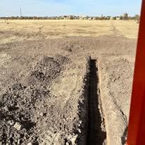 Dry dirt field with a narrow trench or furrow running through the foreground under a clear sky