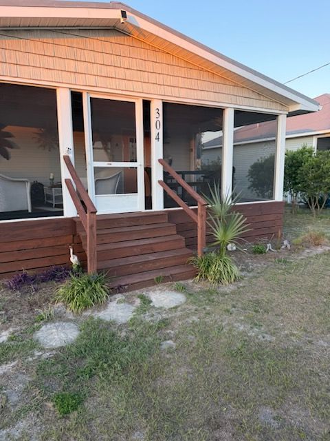 Small porch with steps and railing on a peach house, number 304, with lawn in front.