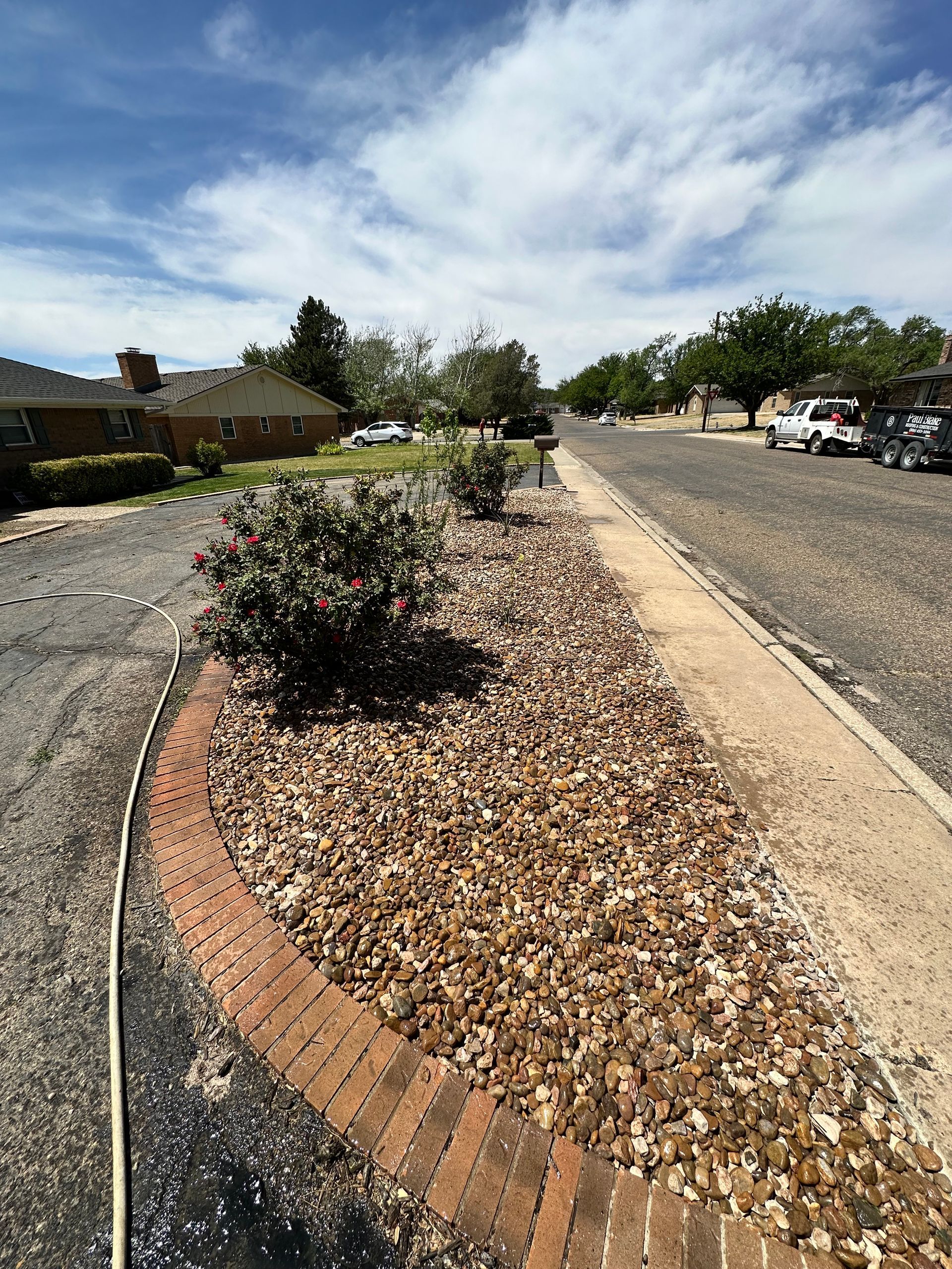 Desert street median with rocks and shrubs under a blue sky, lined by houses and parked cars