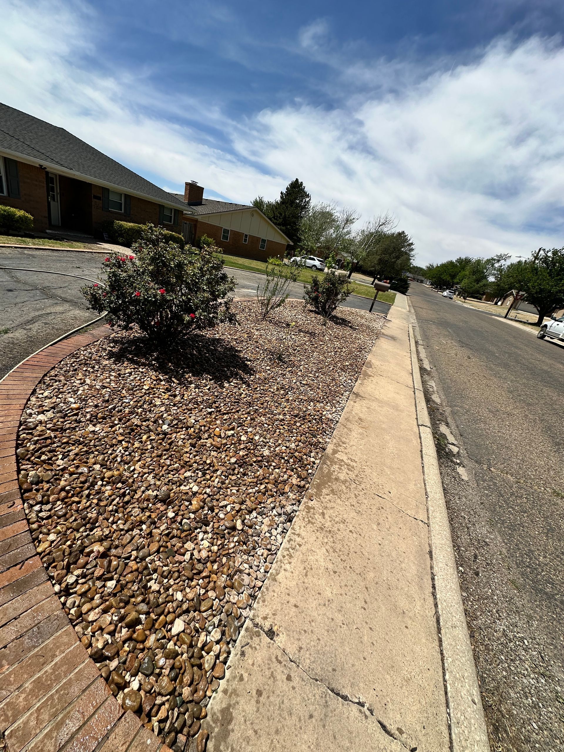 Residential street with gravel landscaping, sidewalk, and cloudy sky along a sloped curb