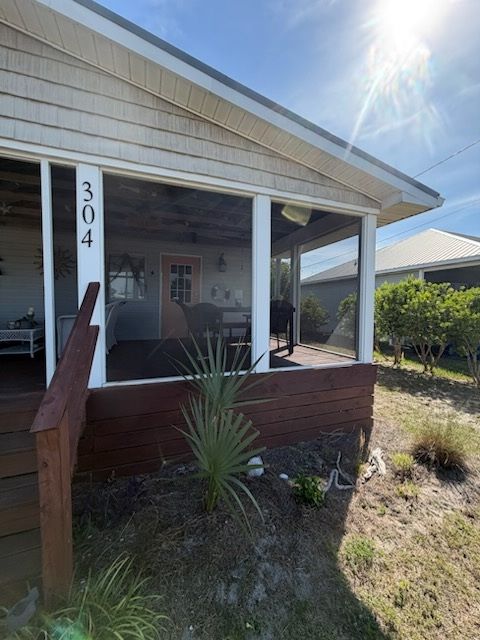 Front porch of a house with the number 304, white posts, brown railing, and bright sun overhead.