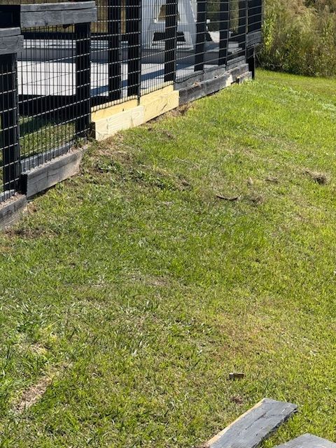 Grassy slope beside a black metal fence and building, with a concrete block near the foreground.