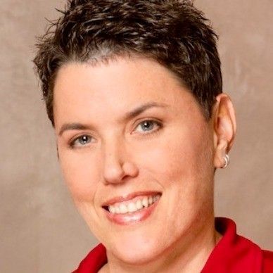 Smiling person with short dark hair wearing a red shirt against a beige background