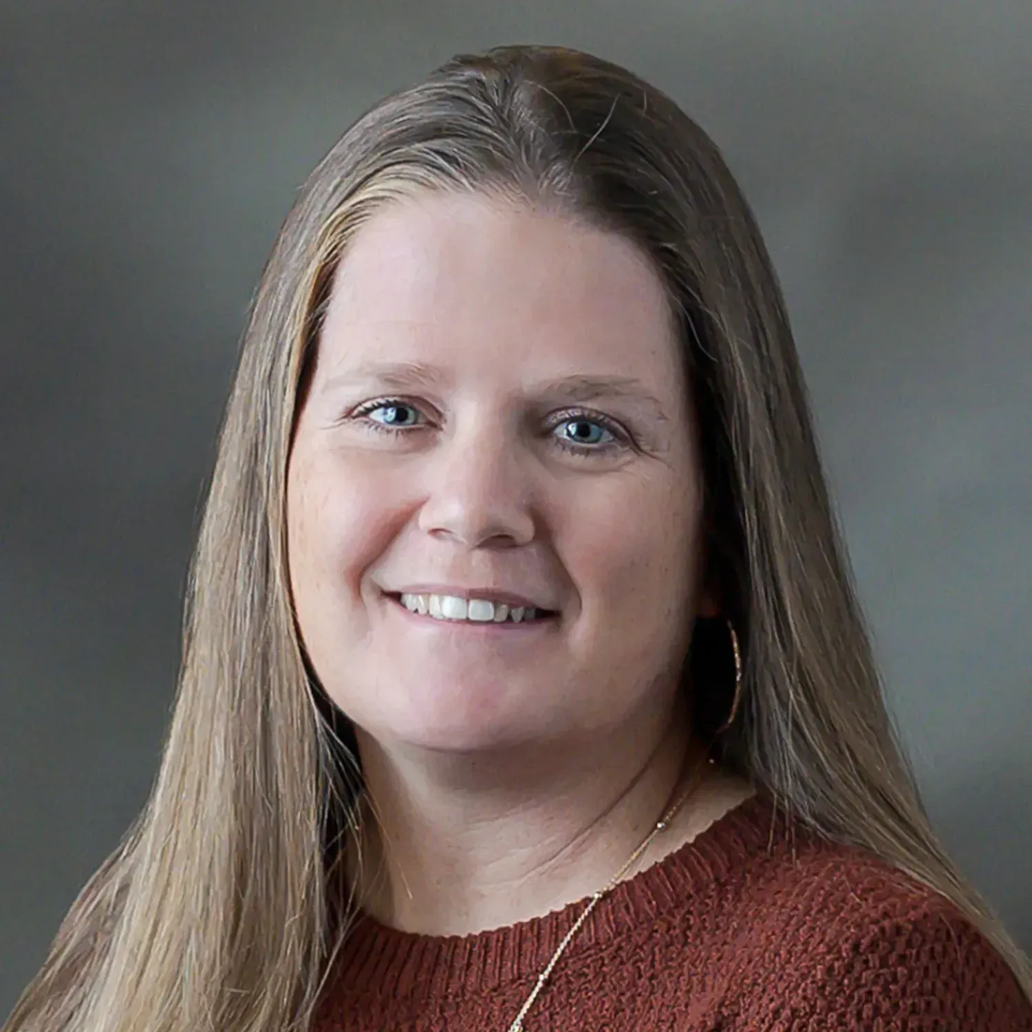 A woman in a brown sweater is smiling for the camera.