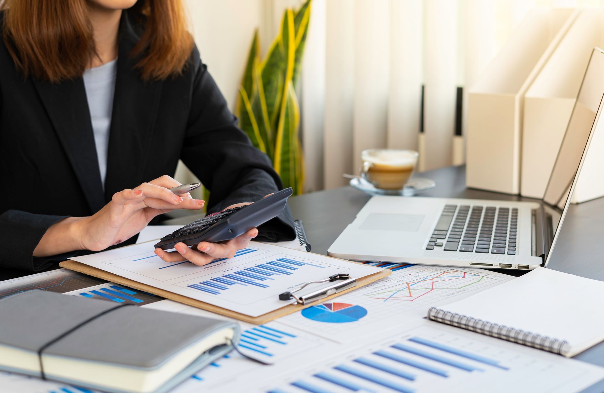 A woman is sitting at a desk using a calculator.