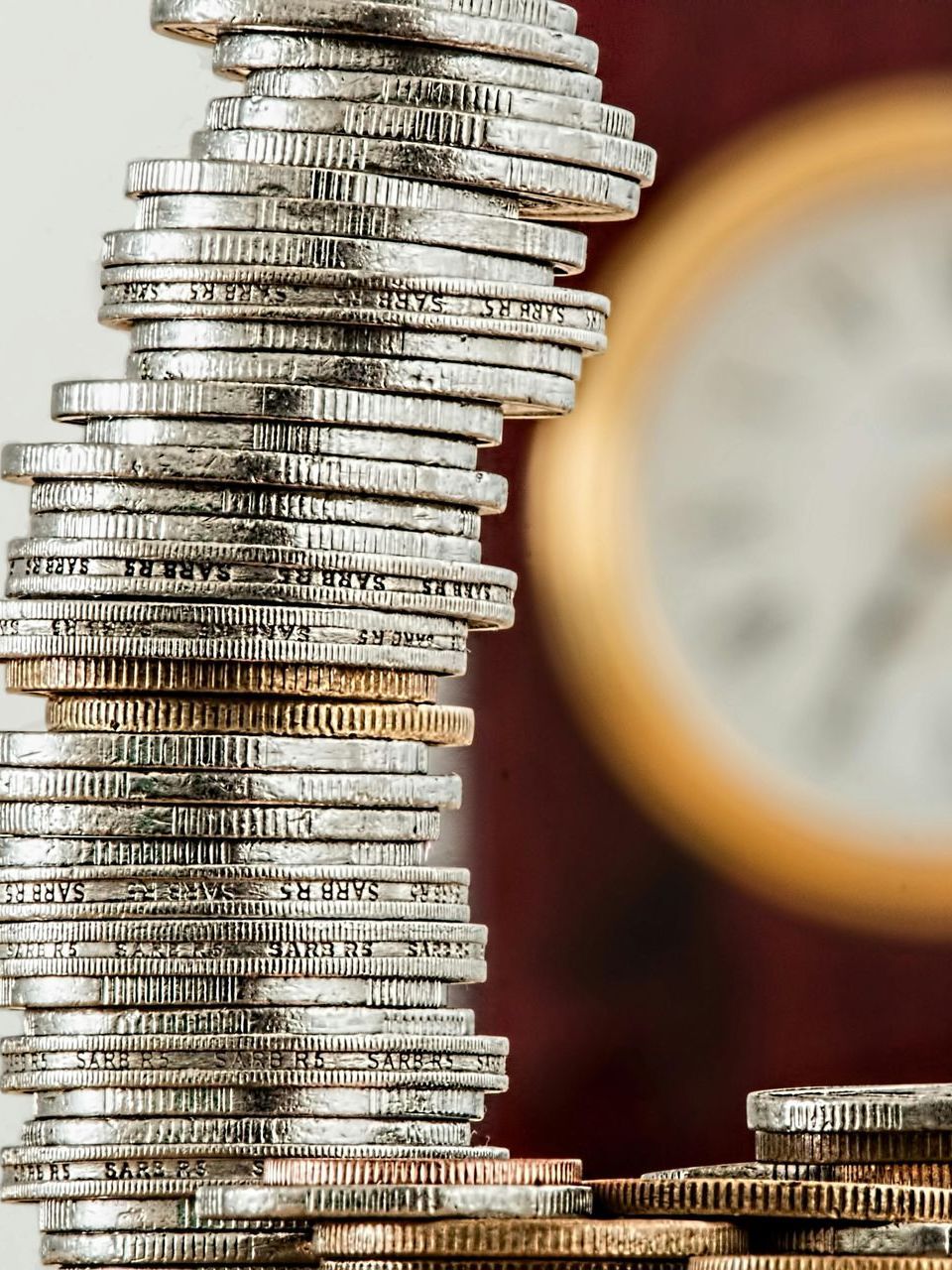 A stack of coins with a clock in the background