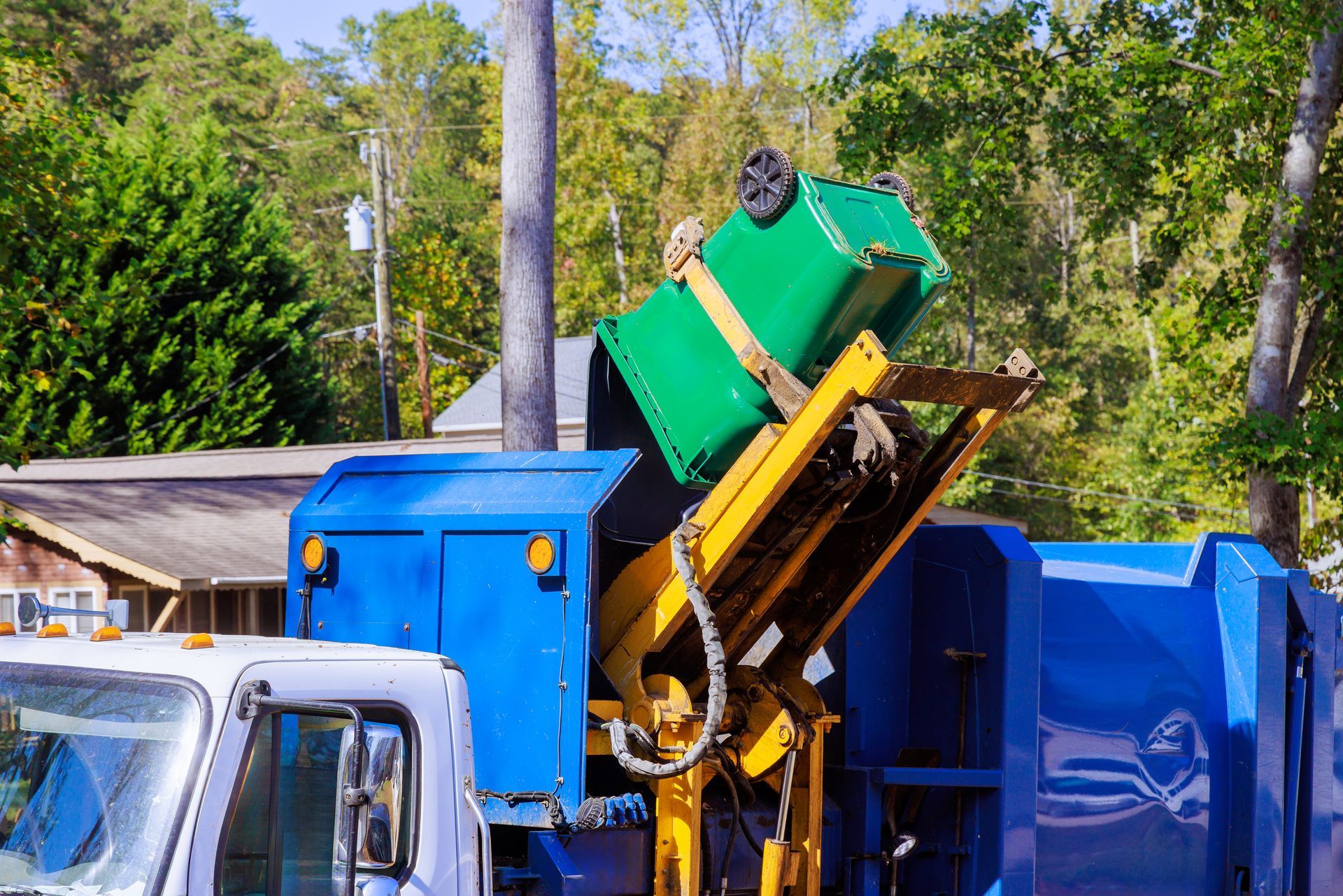 A garbage truck is loading a green trash can into the back of it.