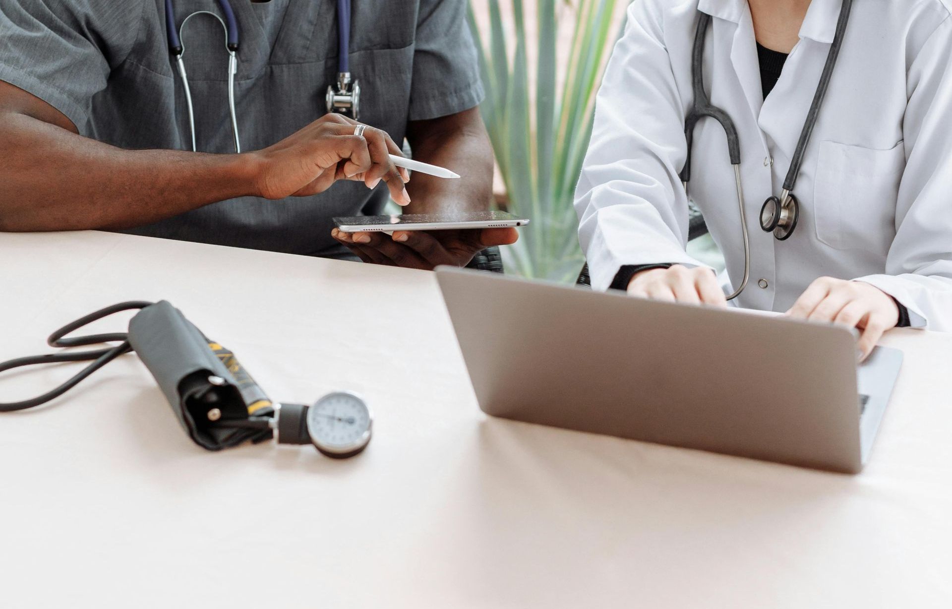 Two doctors are sitting at a table looking at a laptop computer.