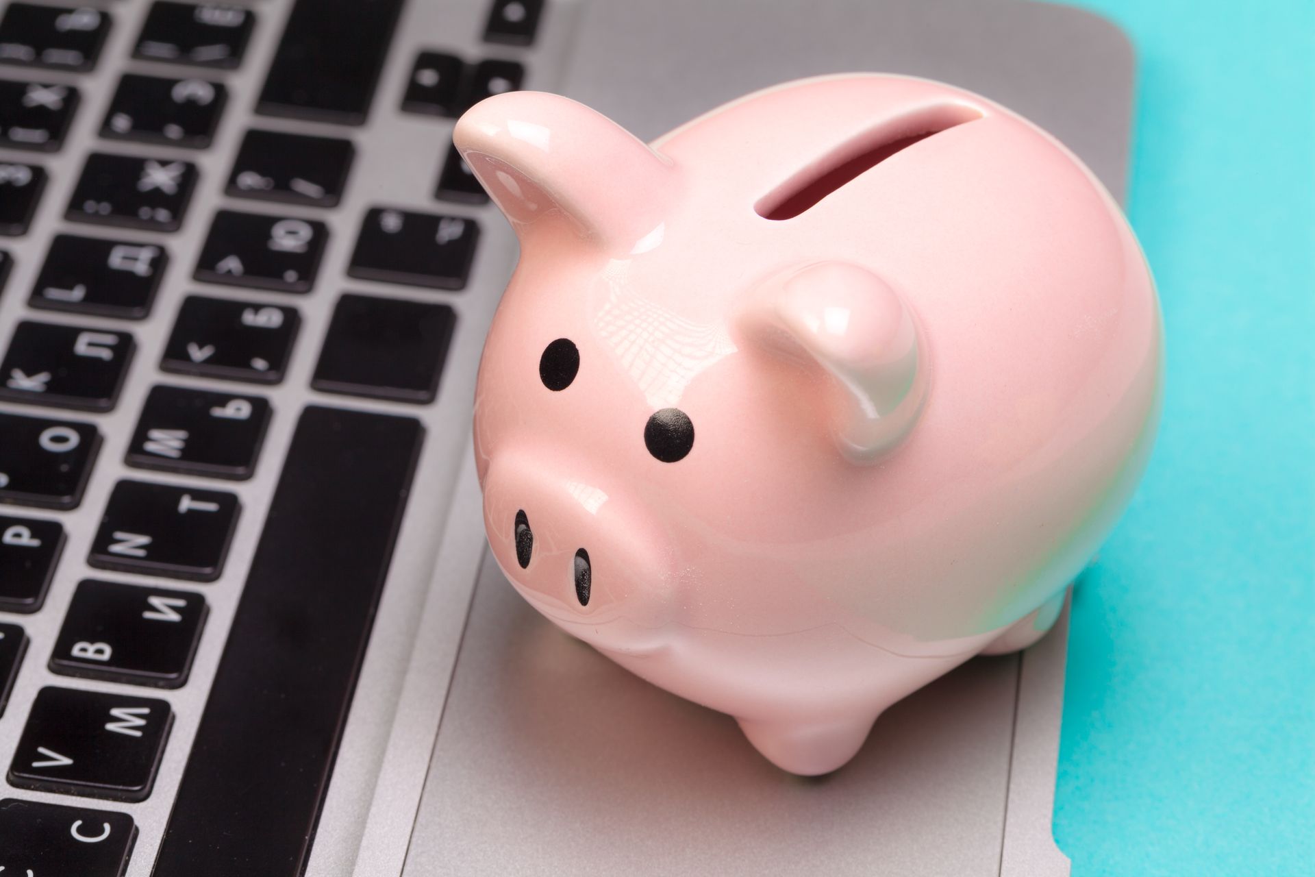 A pink piggy bank is sitting on top of a laptop keyboard