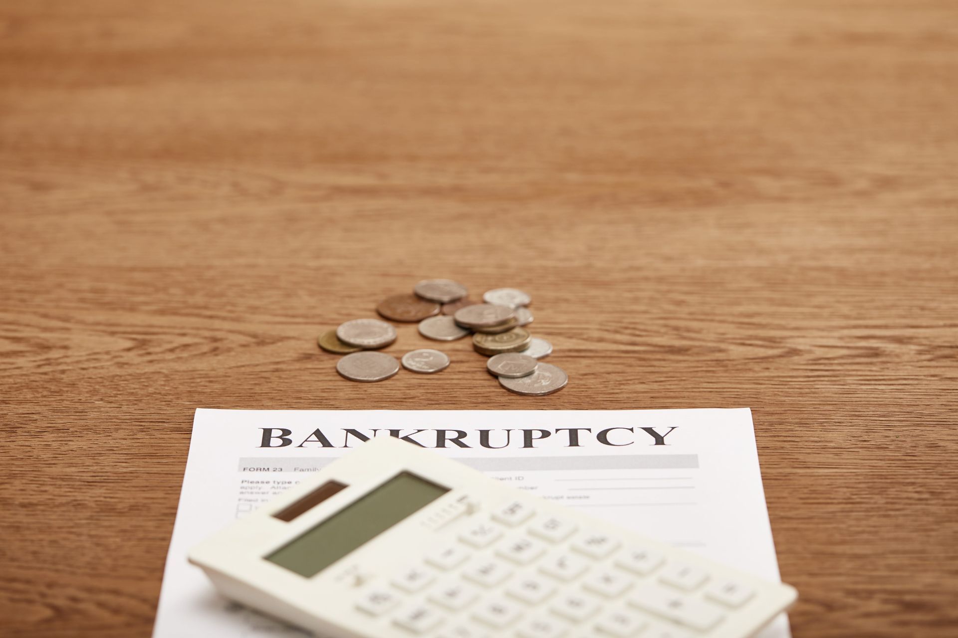 Bankruptcy form with calculator and scattered coins on a wooden desk