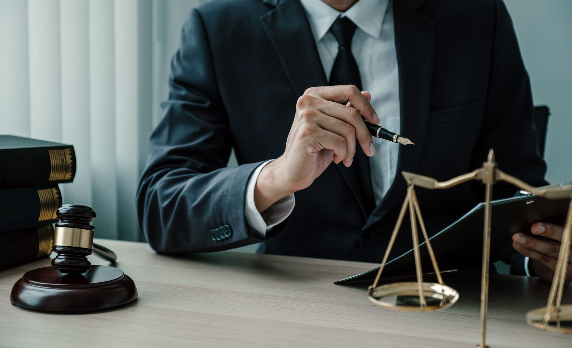 Lawyer in a dark suit at a desk, signing documents beside a balance scale and gavel