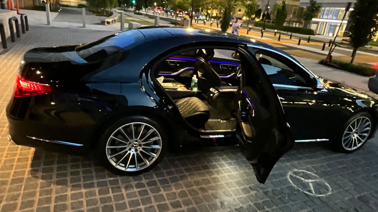 A black mercedes benz with its doors open is parked on a sidewalk.