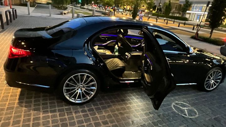 A black mercedes benz with its doors open is parked on a sidewalk.