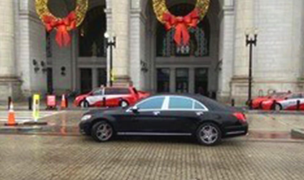 A black car is parked in front of a building decorated for christmas