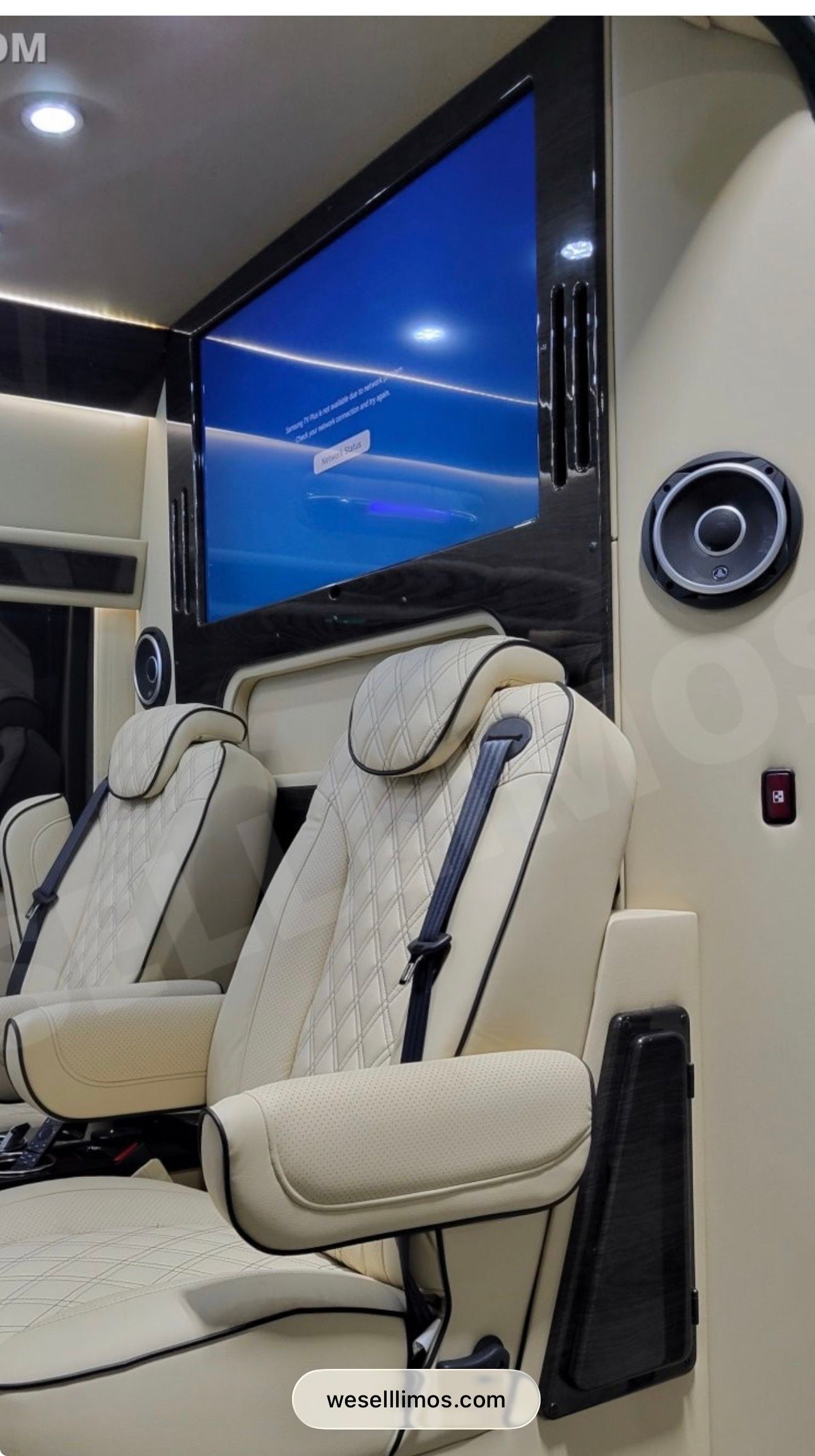 Luxury white leather captain's chairs inside a vehicle, positioned below a large mounted television screen.