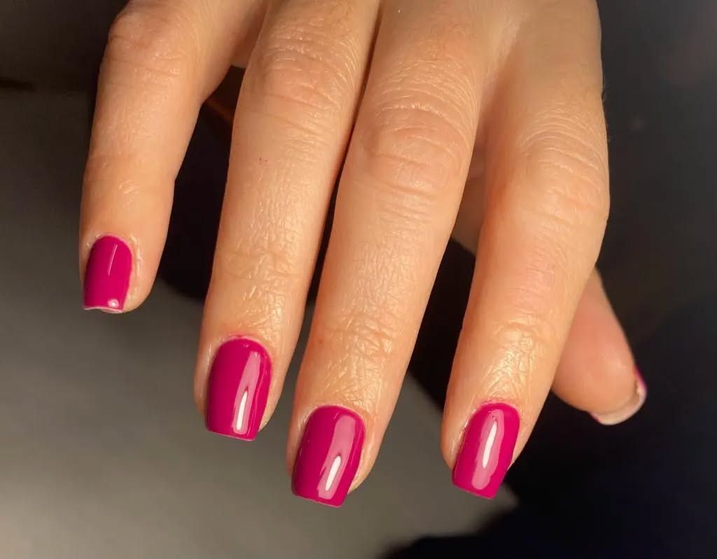Un primo piano delle unghie di una donna con smalto rosa.
