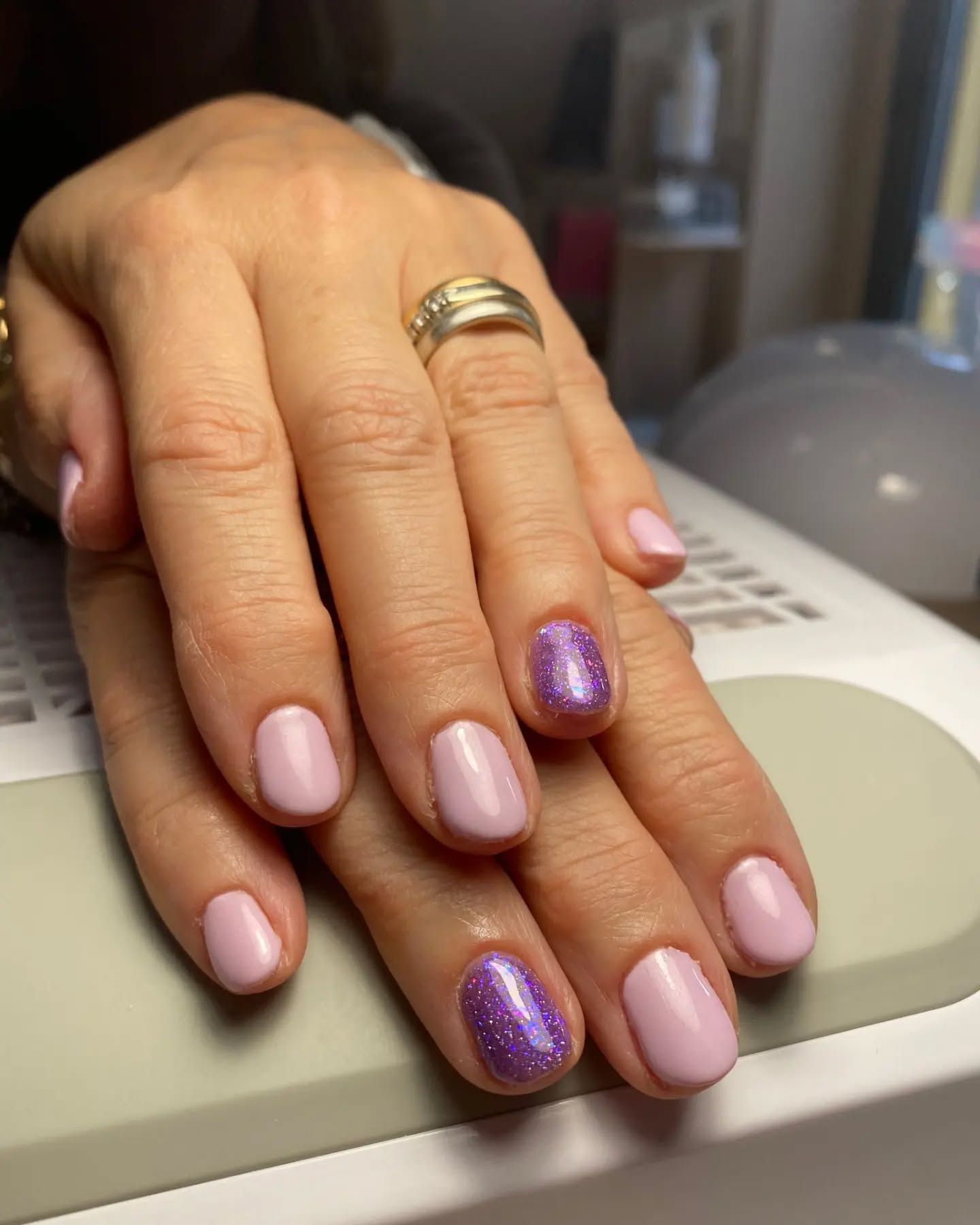 Le mani di una donna con le unghie rosa e viola e un anello al dito.
