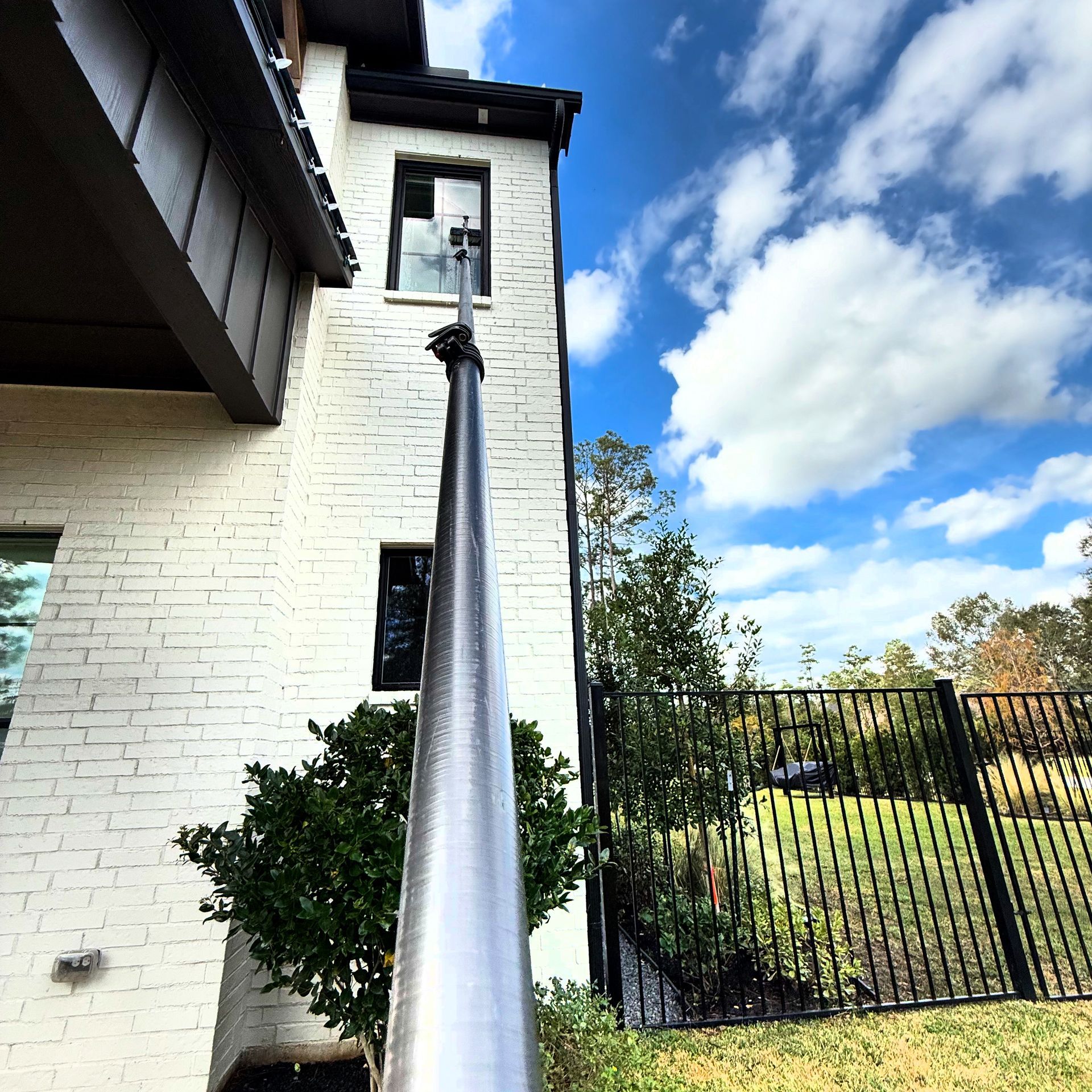 Black handrail beside a white brick house, leading toward a gated yard under a blue sky with clouds