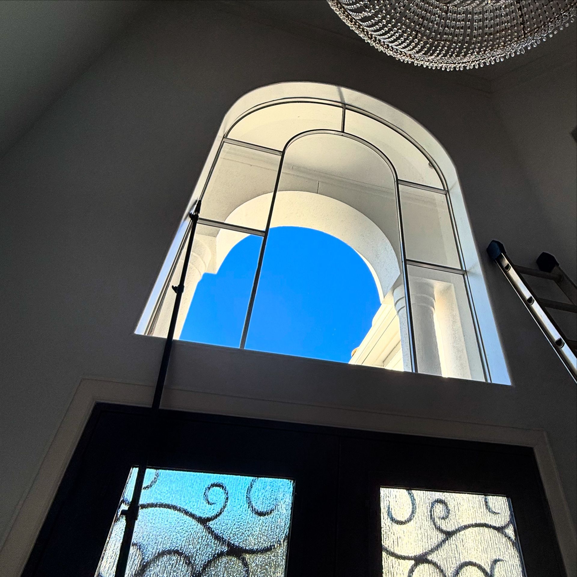 Looking up a bright blue sky through an arched window above a doorway, with a mirrored disco ball ceiling light