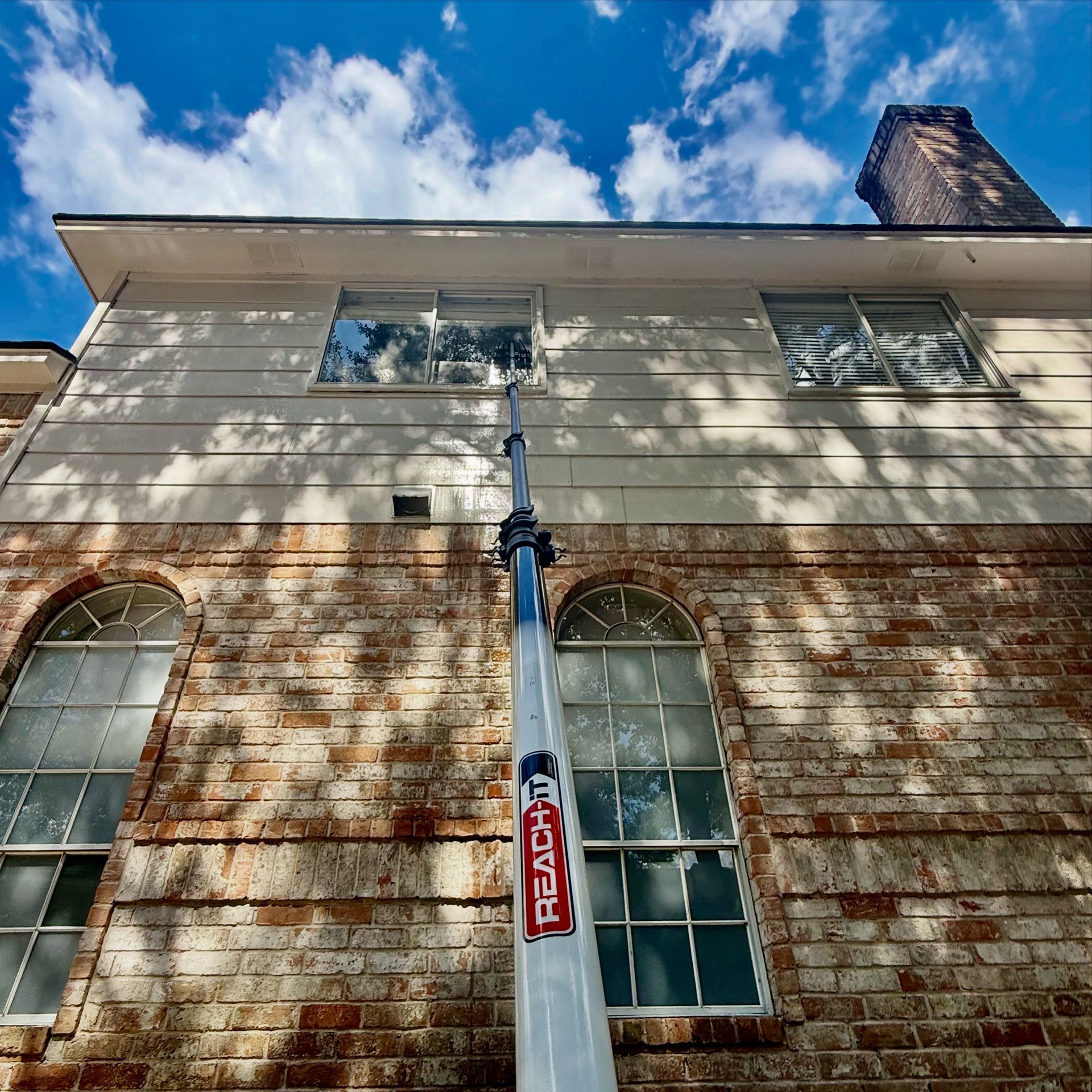 Brick building facade with tall windows and a blue sky with clouds above