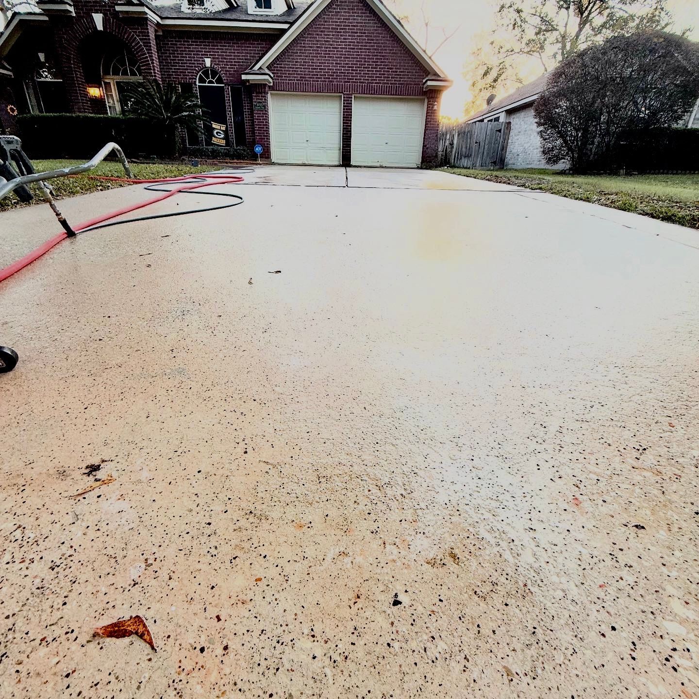 Concrete driveway in front of a garage, with a garden hose on the left and sunlight casting shadows.