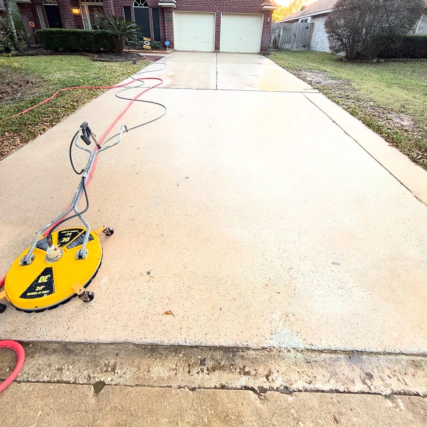 Yellow floor grinder on a concrete driveway leading to a house garage