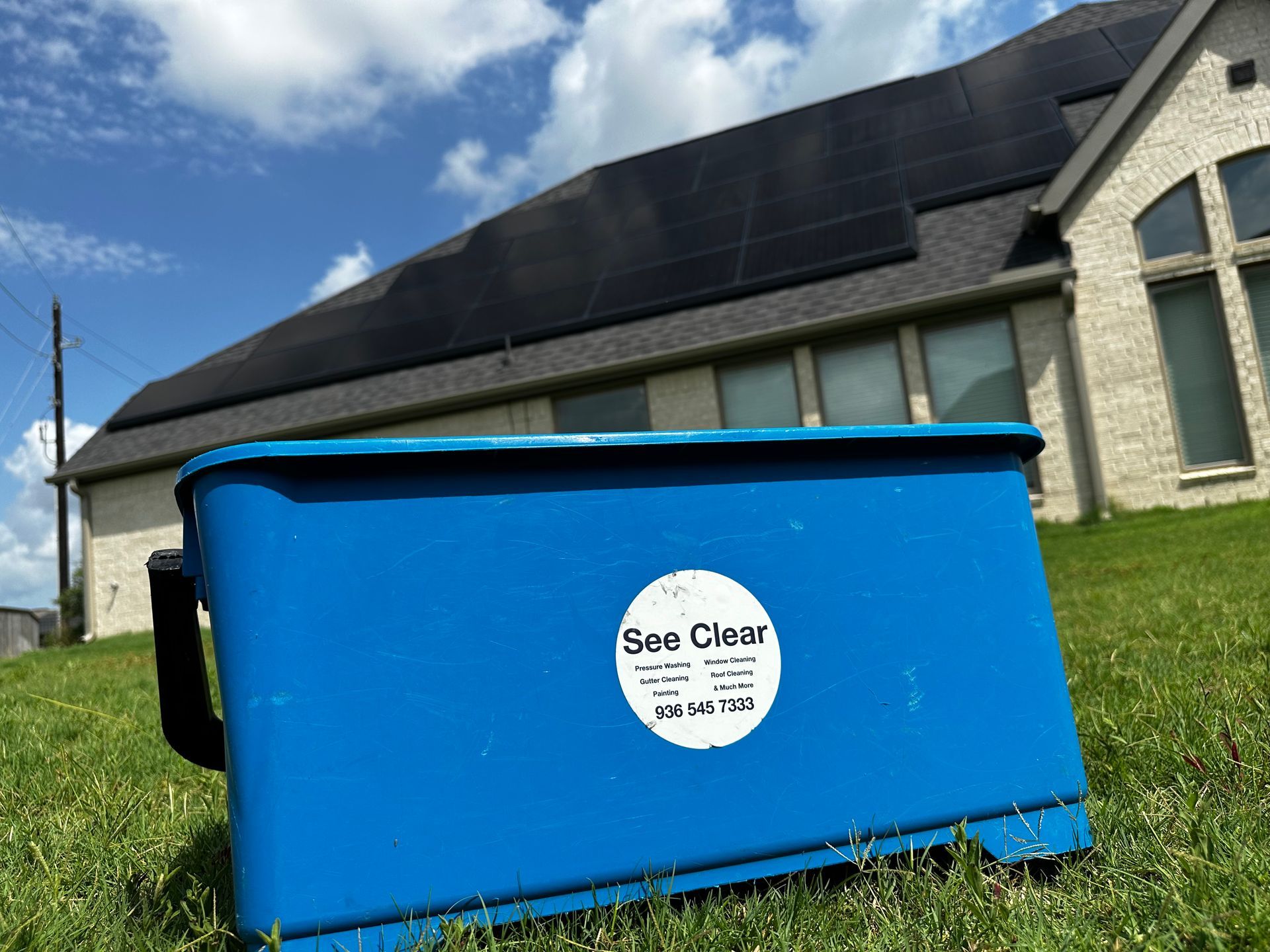Blue Ben Clean bin in a grassy yard beside a house under a partly cloudy sky