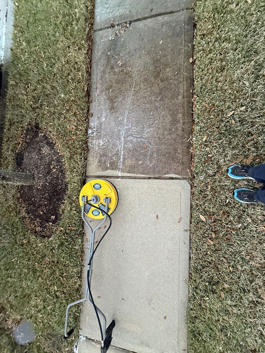 Yellow measuring device on a sidewalk beside grass, next to a concrete path and a shoe.