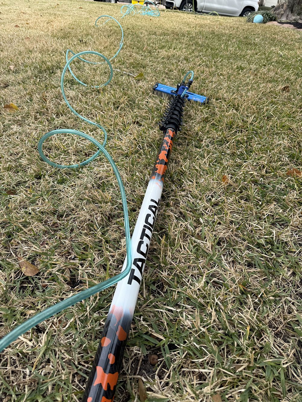 Blue hose and black-orange yard tool handle on grass with fallen leaves