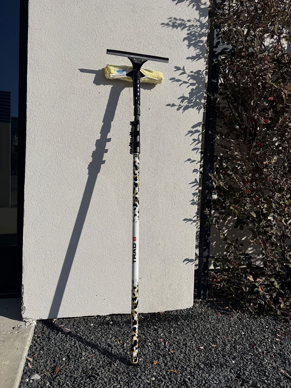 Tall scooter leaning against a white wall beside dark gravel and bushes.