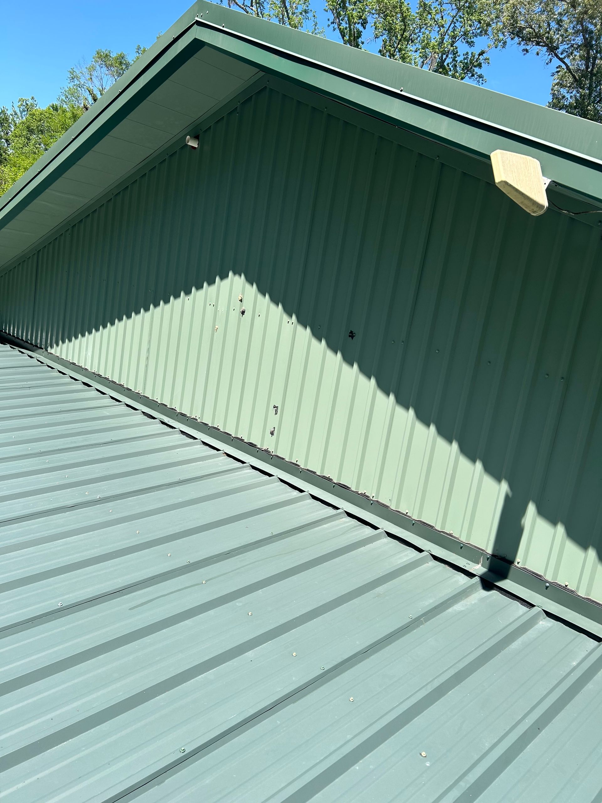 Green metal roof and gable wall beneath a blue sky, viewed from below