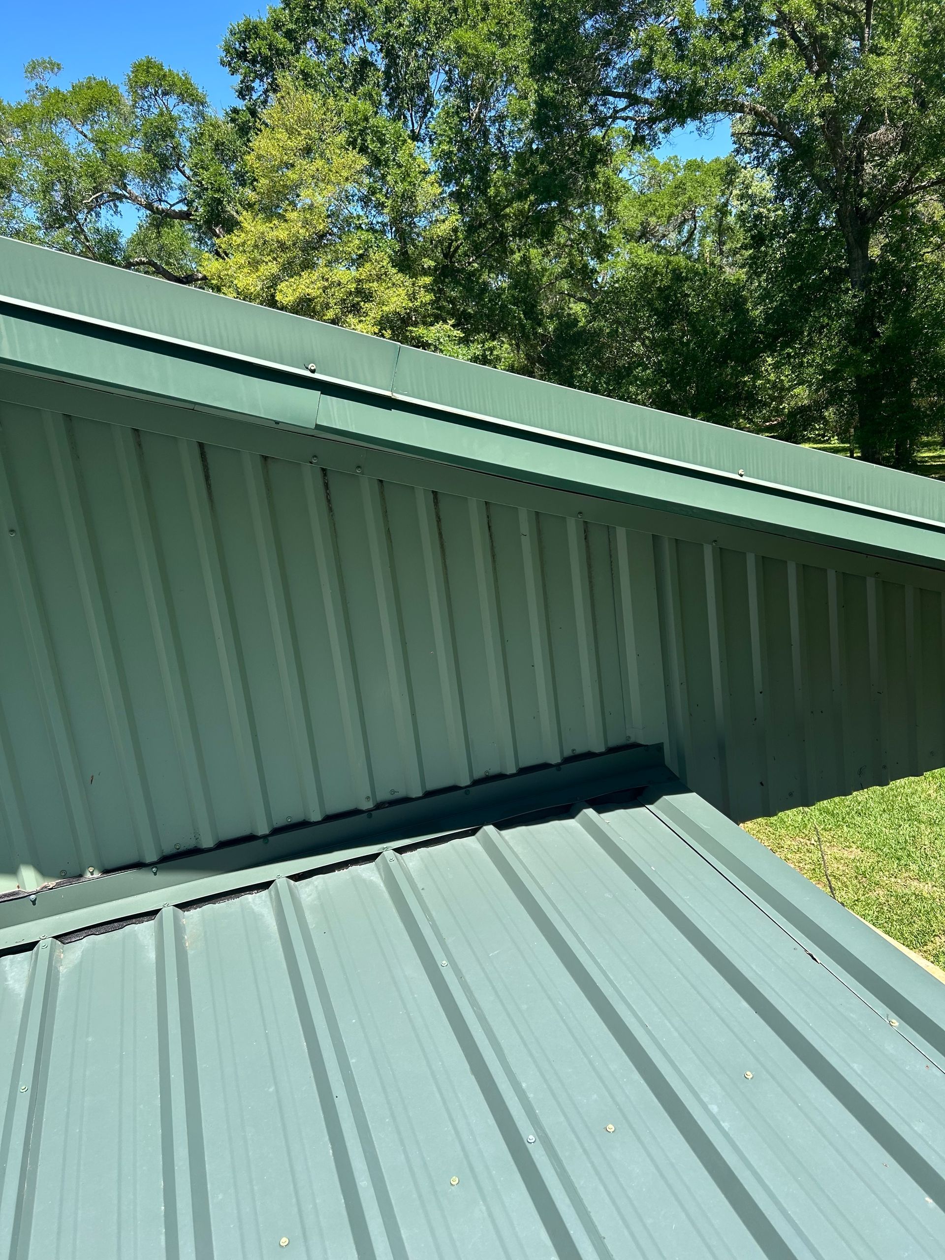 Green metal roof with a lower roof section and trees in the background