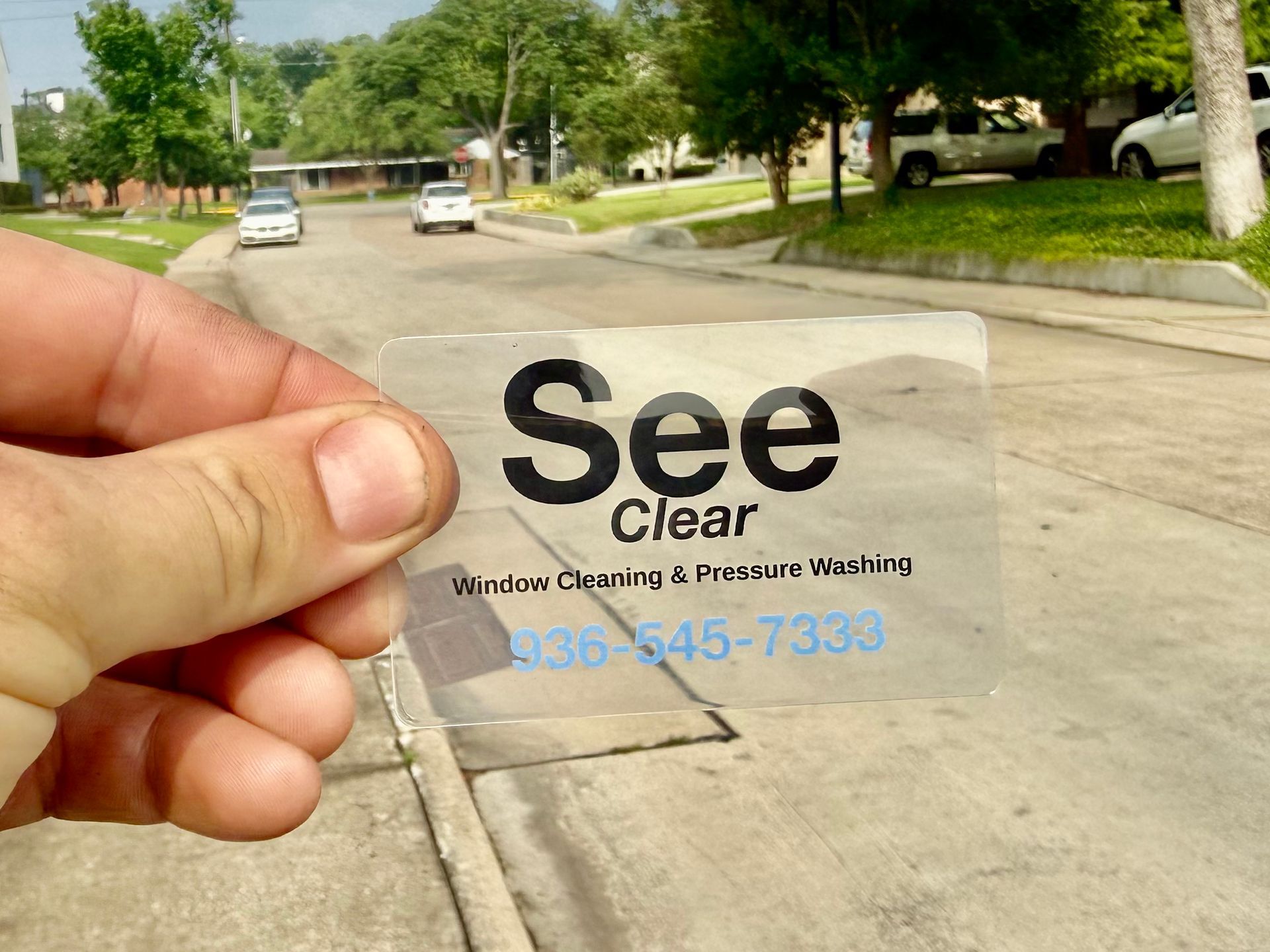 Hand holding a Clear View window cleaning business card on a suburban street.