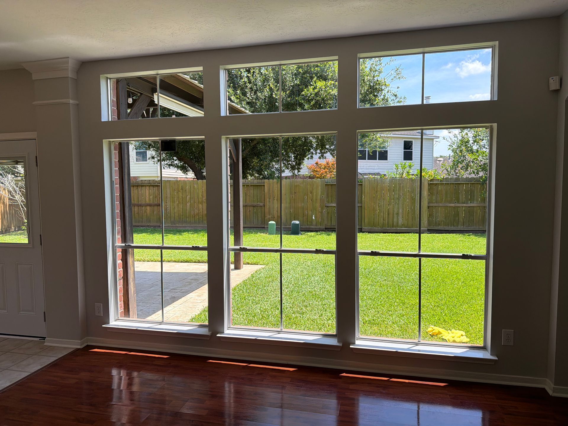 Bright living room with hardwood floors and large windows overlooking a sunny fenced backyard.