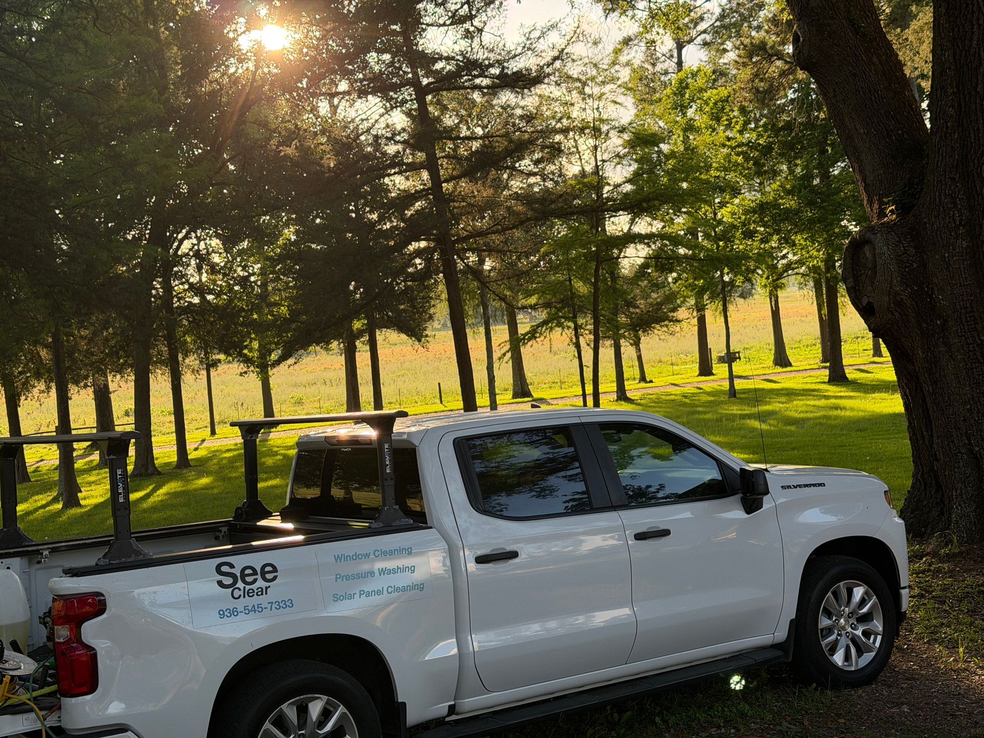 White pickup truck with a sign parked by a lakeside road under trees at sunset