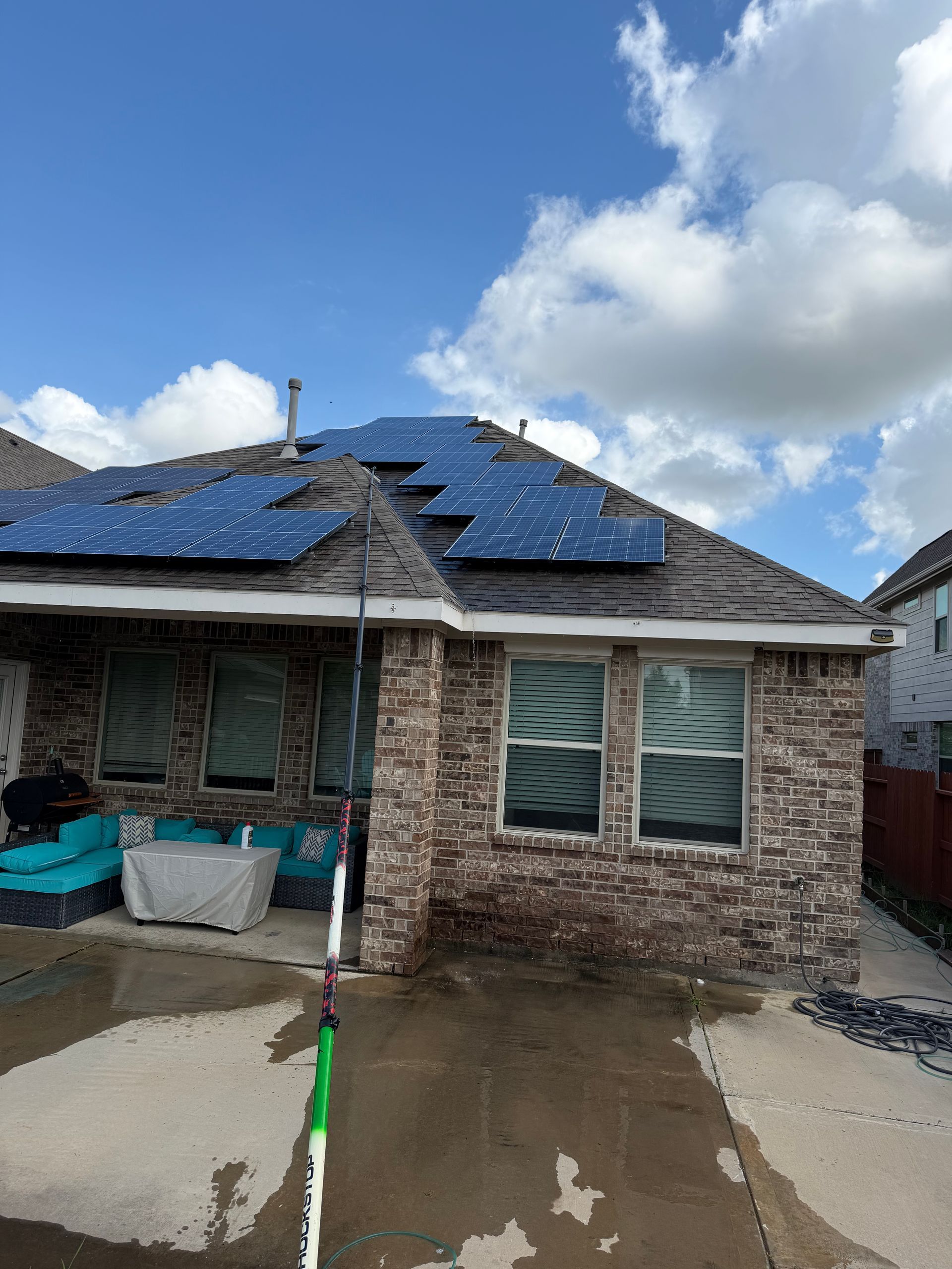 House with damaged blue roof tiles and wet driveway under cloudy sky