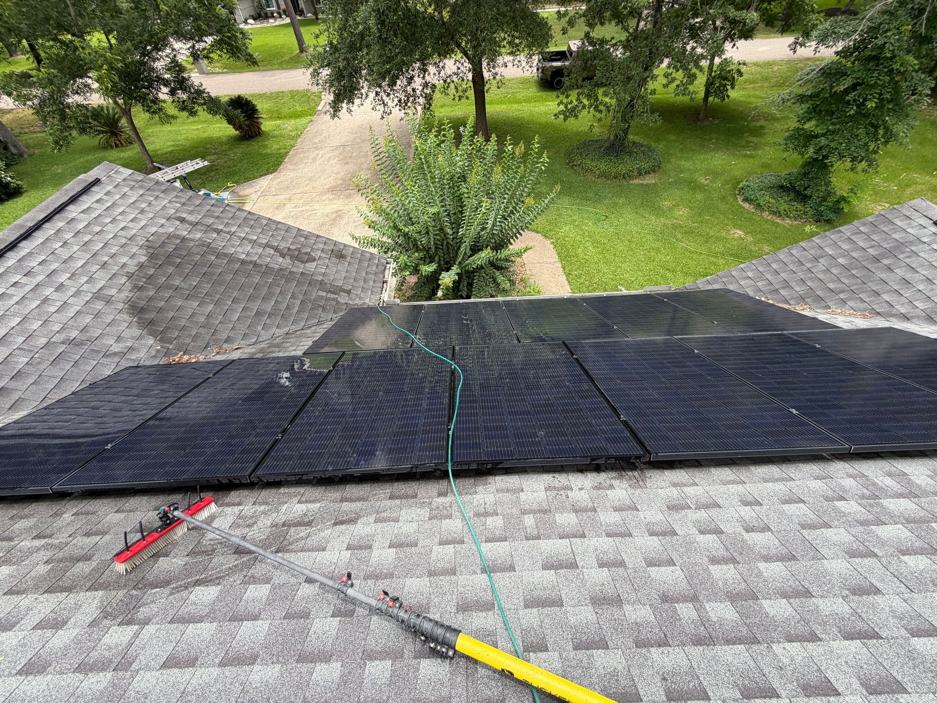 Workers repairing a rooftop with black solar panels and tools, overlooking a green yard below