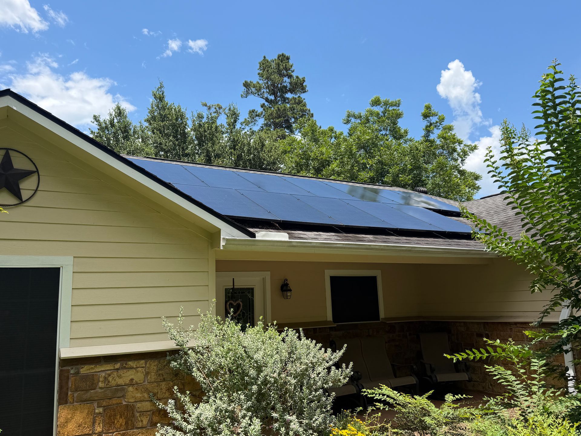 House with solar panels on the roof, viewed from the yard under a blue sky.